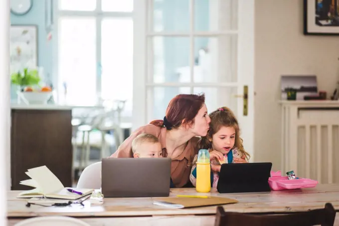 Mid adult woman kissing daughter while sitting with son at home