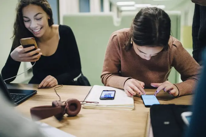 Female high school students using smart phone at desk in classroom