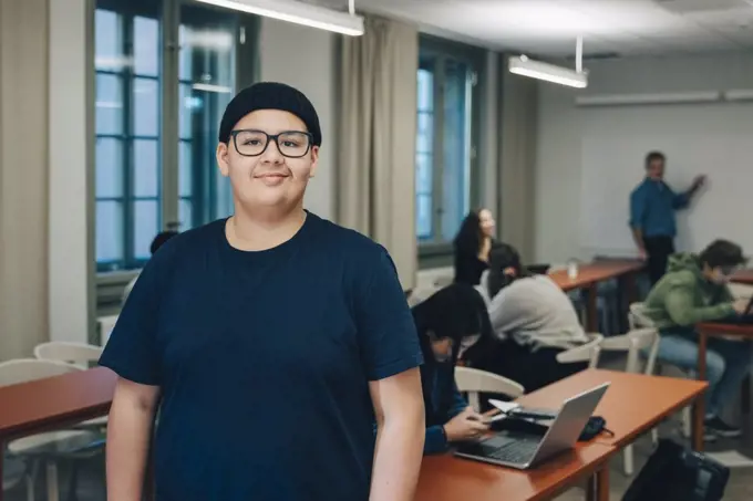 Portrait of teenage boy with classmates at desk in classroom