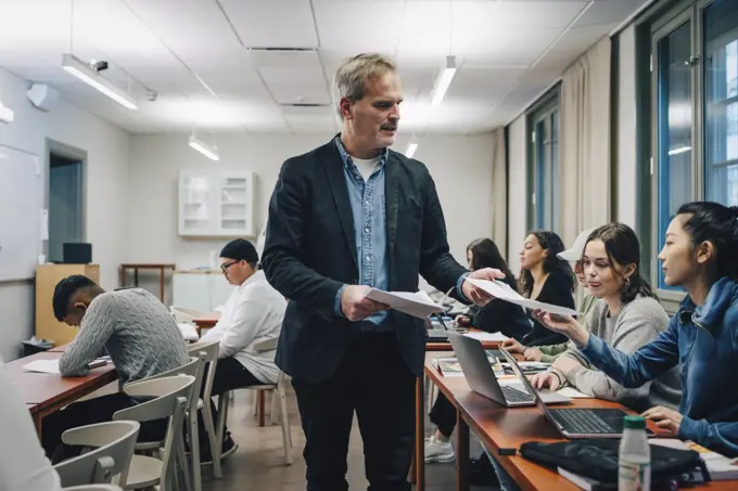 Teacher giving questionnaire to students sitting at desk in classroom