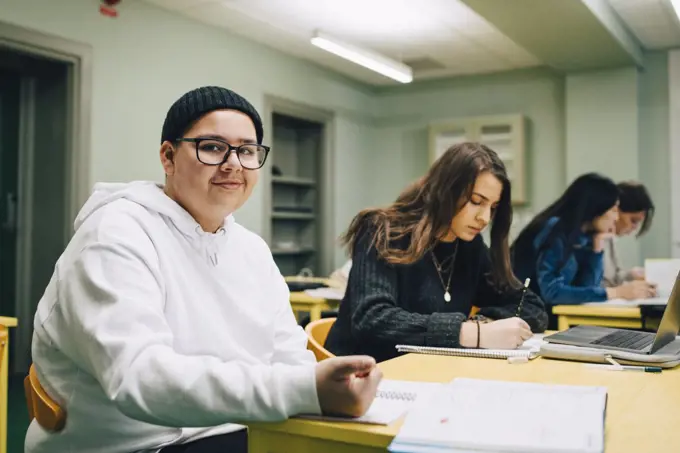 Portrait of smiling male high school student sitting by classmate in classroom