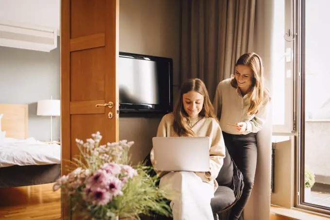 Happy friends shopping online with credit card through laptop in hotel room during vacations