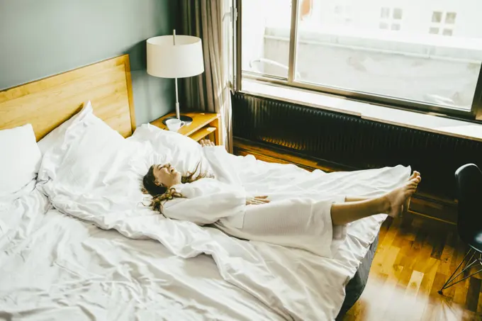 Smiling woman in bathrobe having fun on bed at hotel room