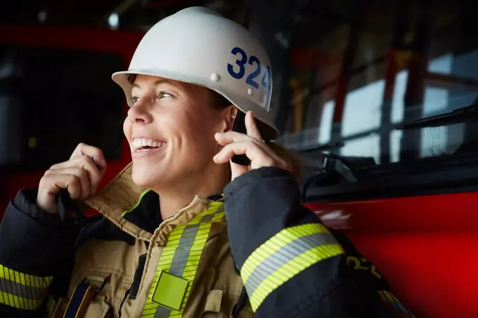 Smiling female firefighter wearing helmet at fire station