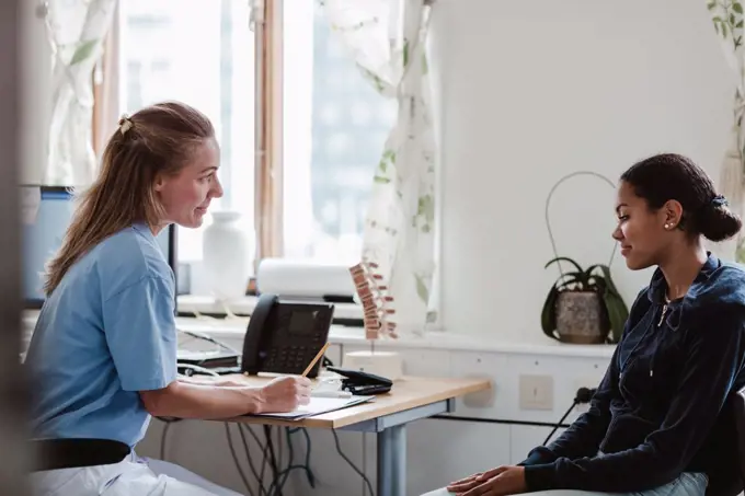 Mature nurse explaining to female patient while sitting at doctor's office