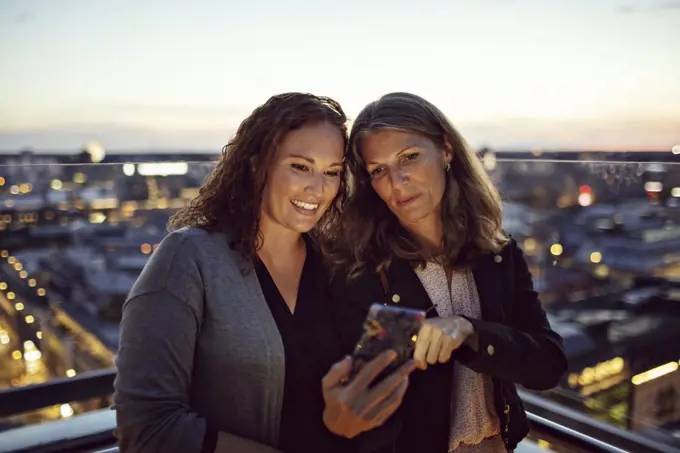 Businesswomen taking selfie on smart phone while standing on terrace after work