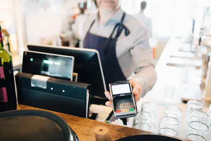 Midsection of man holding credit card reader in restaurant