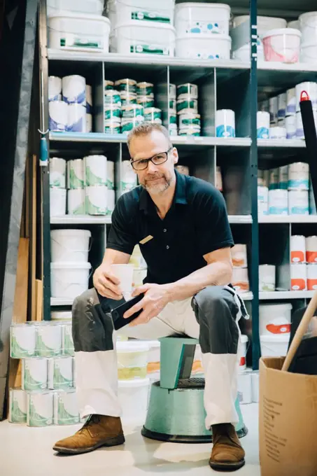 Full length of portrait of salesman sitting on stool in storage room