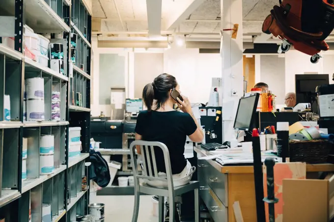 Rear view of sales woman using phone while sitting at counter in hardware store