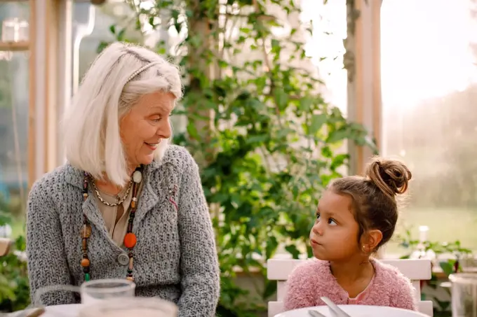 Smiling grandmother looking at granddaughter while having lunch