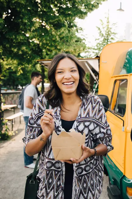 Female customer laughing while standing with box near food truck