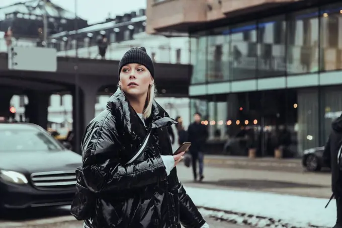 Young woman wearing warm clothing while looking away on street in city during winter