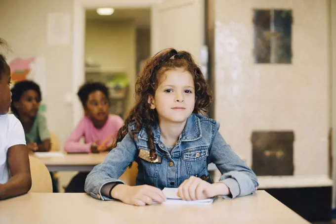 Portrait of smiling schoolgirl sitting with friends at desk in classroom