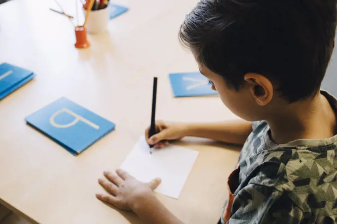 High angle view of schoolboy practicing alphabets at table in classroom