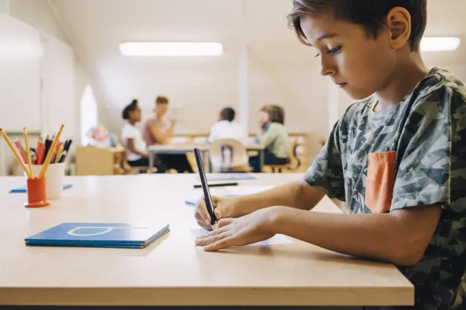 Close-up of boy concentrating while writing on paper at table