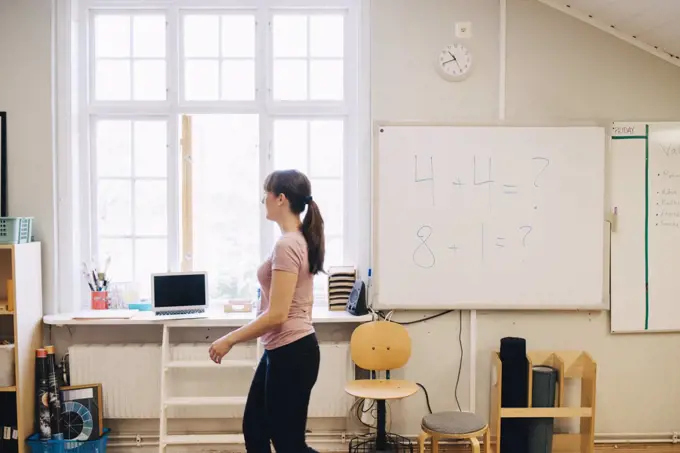 Side view of teacher walking by whiteboard with mathematics in classroom