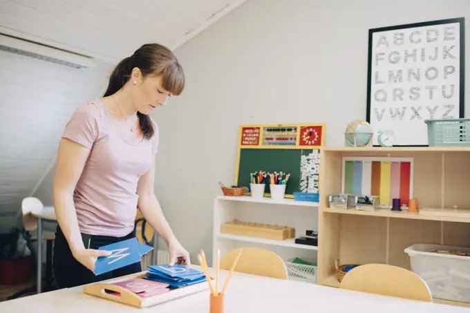 Confident mid adult female teacher arranging flash cards with alphabets at table in classroom