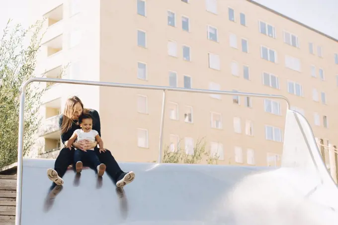 Mother playing with daughter on slide at park in city