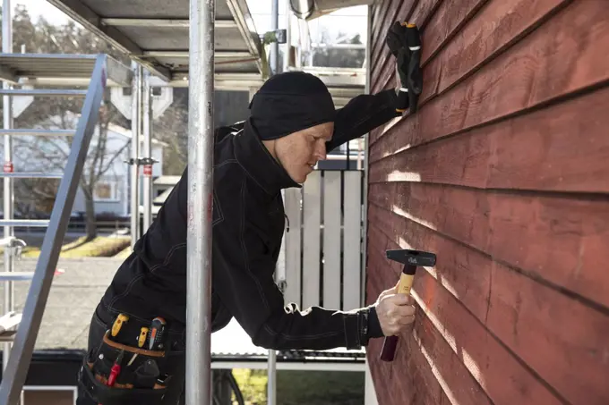 Side view of confident repairman hammering wooden wall at construction site