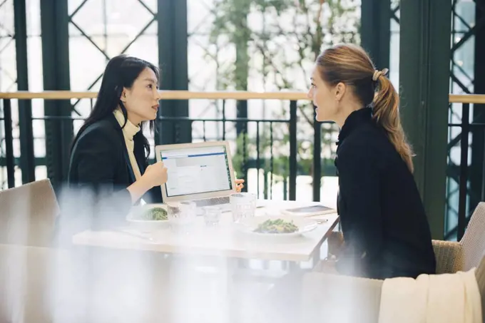 Confident multi-ethnic female business colleagues discussing over laptop at cafeteria