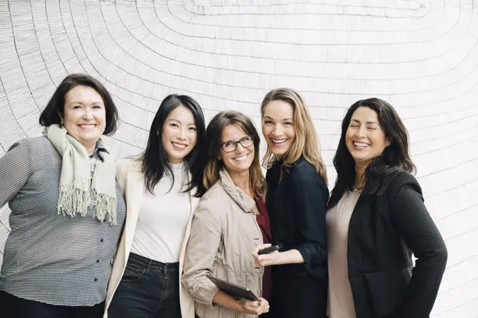 Portrait of smiling multi-ethnic businesswomen standing against wall at workplace