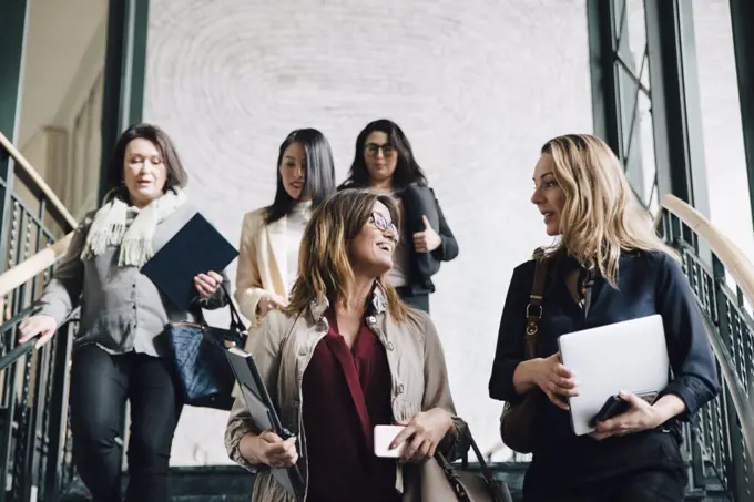 Low angle view of multi-ethnic female entrepreneurs moving down on staircase in office