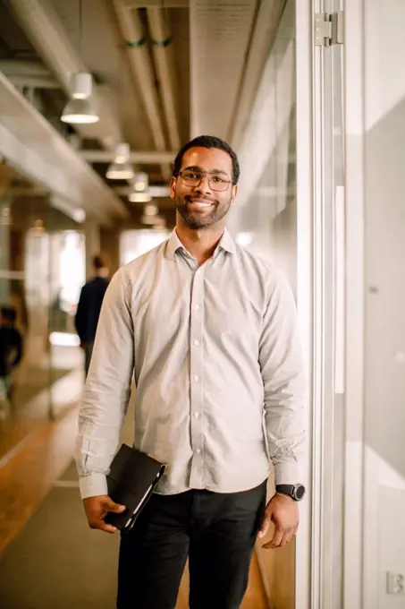 Portrait of smiling mid adult businessman holding digital tablet in office corridor