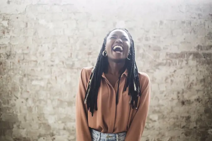 Female computer hacker with dreadlocks laughing against wall in office