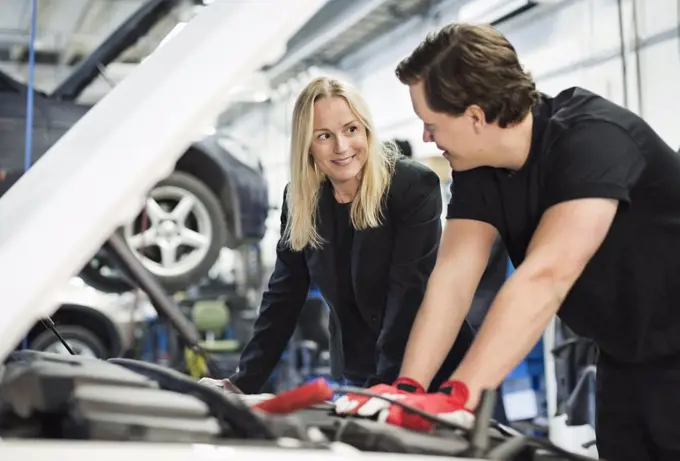 Male mechanic discussing with female customer while repairing car engine at workshop