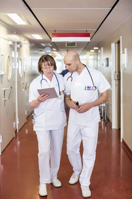 Male and female doctors using digital tablet while walking in hospital corridor