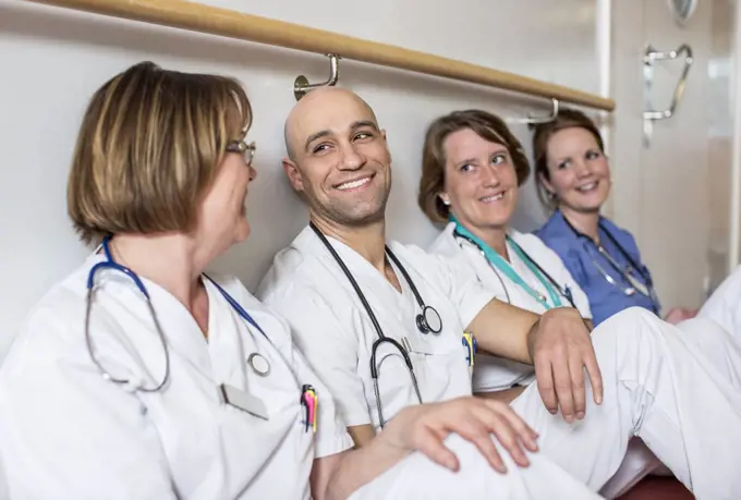 Happy male doctor and female colleagues leaning together on wall in hospital