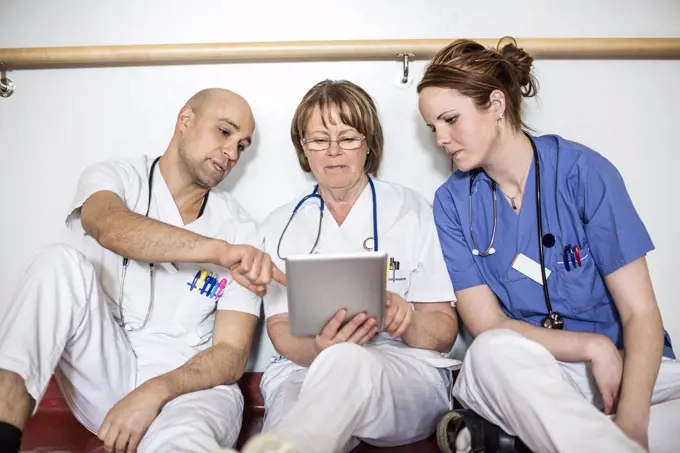 Doctors using digital tablet while leaning on wall in hospital