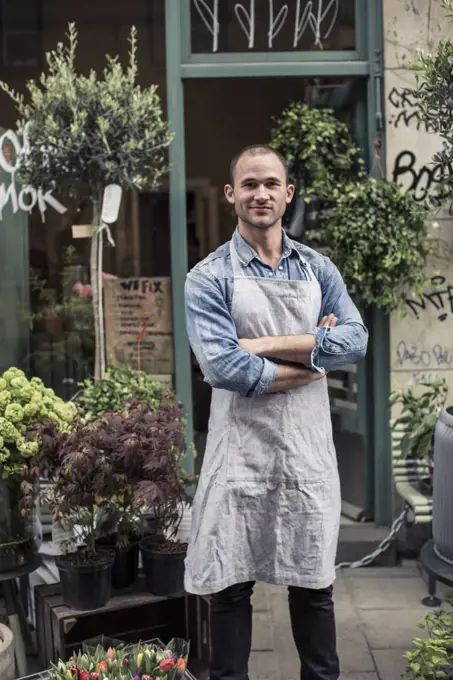 Portrait of confident male florist standing arms crossed outside flower shop