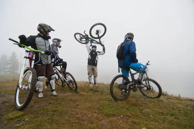 Friends looking at man picking up bicycle on mountain