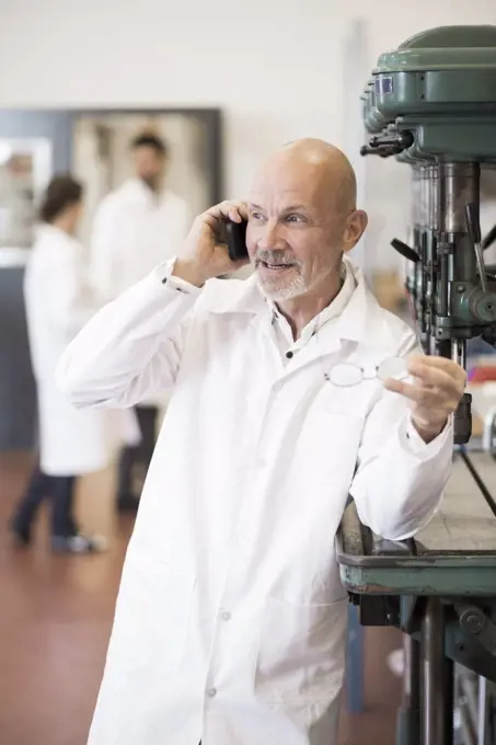 Engineer answering mobile phone with colleagues in background at industry