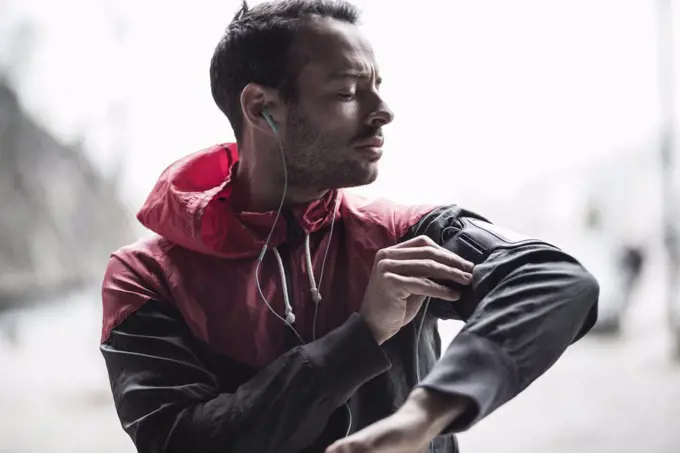 Sporty man adjusting arm band while listening to music