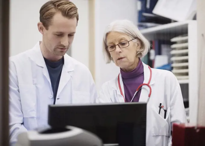 Senior female doctor with male colleague using computer in examination room