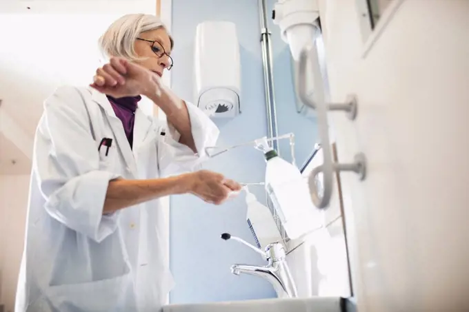 Low angle view of senior female doctor using soap dispenser to wash hands in bathroom