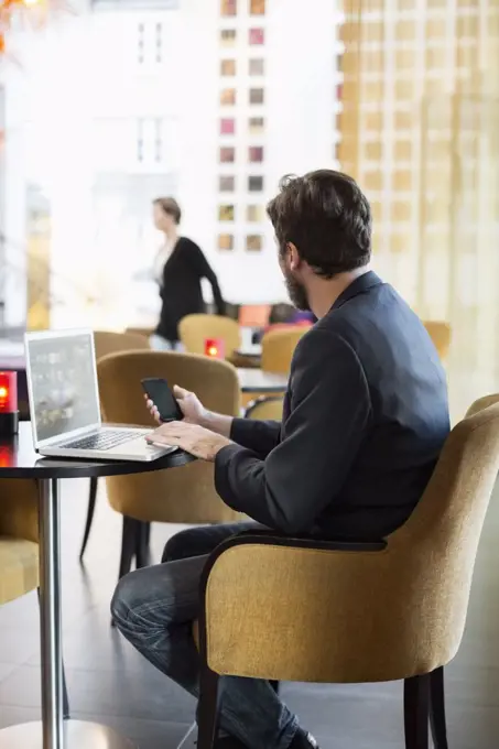 Side view of businessman with mobile phone and laptop sitting in hotel restaurant