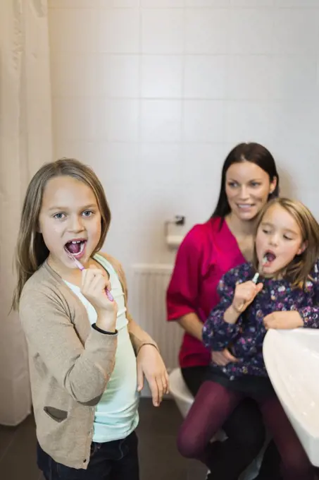 Portrait of girl brushing teeth with mother and daughter in bathroom