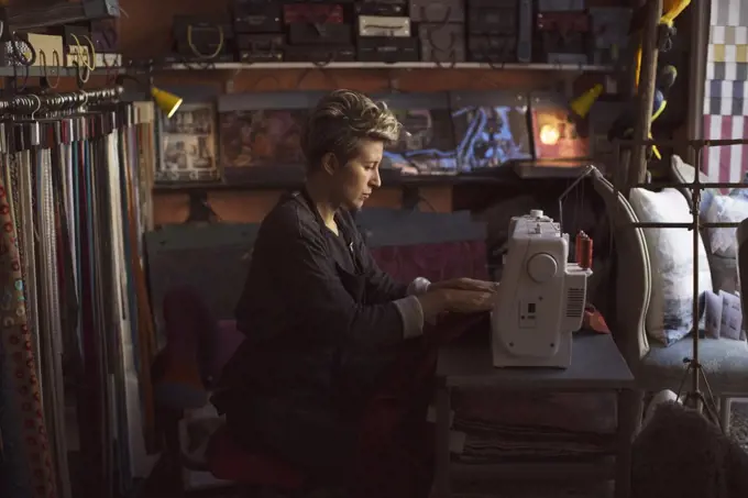 Side view of female fashion designer using sewing machine in studio