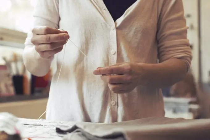 Midsection of woman threading needle while standing at table