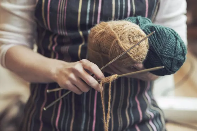 Midsection of woman holding knitting tools at home