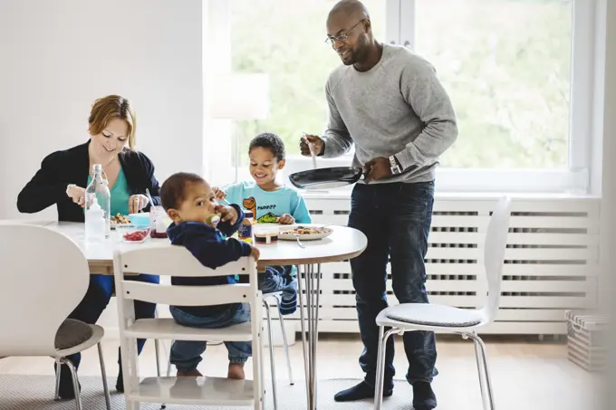 Man serving food to family at dining table in house