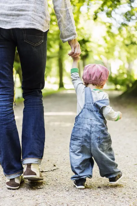 Rear view of baby girl holding mother's hand while walking on dirt road