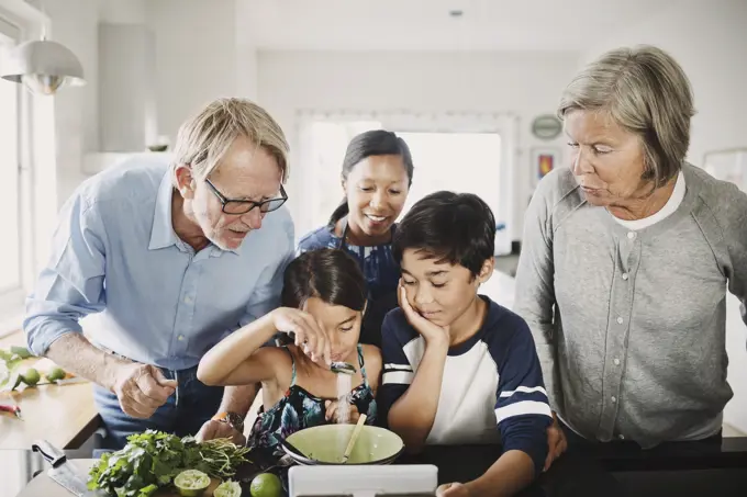 Family looking at girl preparing food at kitchen counter