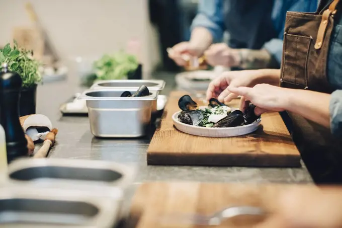 Midsection of female chefs preparing food on counter in restaurant kitchen