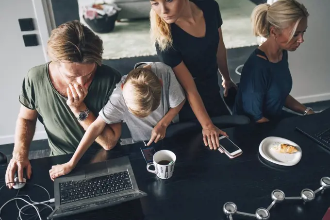 High angle view of family using technologies at dining table in room