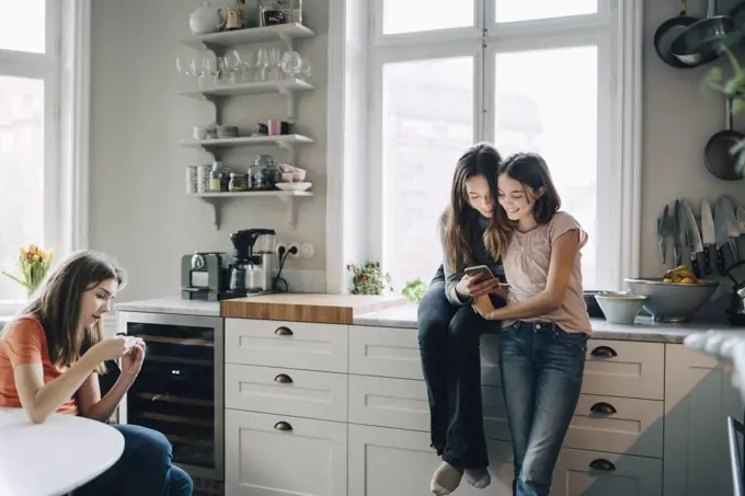 Female friends using mobile phone in kitchen at home