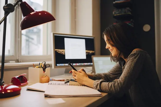 Happy girl using mobile phone while sitting at illuminated desk